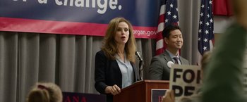 Movie still from “Sweet Girl” (2021), directed by Brian Andrew Mendoza – A woman standing at a podium speaking at a political event; Medium shot, Over the shoulder angle