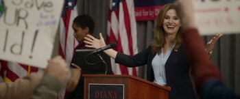 Movie still from “Sweet Girl” (2021), directed by Brian Andrew Mendoza – A woman standing at a podium giving a speech to a crowd; Medium shot, Over the shoulder angle
