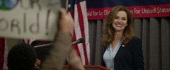 Movie still from “Sweet Girl” (2021), directed by Brian Andrew Mendoza – A woman standing at a podium with a microphone in front of an american flag; Medium shot, Low angle
