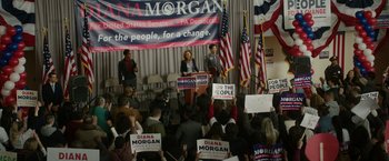 Movie still from “Sweet Girl” (2021), directed by Brian Andrew Mendoza – A woman standing at a podium in front of a crowd of people; Extreme Wide shot, High angle