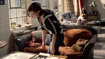 Movie still from “Closer” (2004), directed by Mike Nichols – A woman standing in a living room looking at pictures on a table; Medium shot, High angle