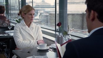 Movie still from “Closer” (2004), directed by Mike Nichols – A woman sitting at a table in front of a window; Medium shot, Over the shoulder angle