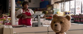 Movie still from “Ted 2” (2015), directed by Seth MacFarlane – A woman standing in front of a counter in a grocery store; Medium shot, Over the shoulder angle