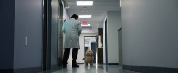 Movie still from “Ted 2” (2015), directed by Seth MacFarlane – A person in a white lab coat standing next to a teddy bear in a hospital hallway; Wide shot, Low angle