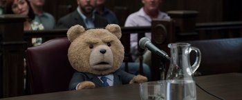 Movie still from “Ted 2” (2015), directed by Seth MacFarlane – A teddy bear in a suit sitting at a table in front of microphones; Medium shot, Low angle