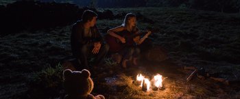 Movie still from “Ted 2” (2015), directed by Seth MacFarlane – A man and a woman sitting in front of a fire with a guitar; Wide shot, Over the shoulder angle