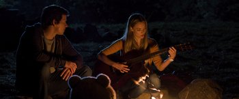 Movie still from “Ted 2” (2015), directed by Seth MacFarlane – A woman playing a guitar in front of a fire; Medium shot, Over the shoulder angle