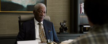 Movie still from “Ted 2” (2015), directed by Seth MacFarlane – An older man sitting at a desk in front of a statue; Close Up shot, Over the shoulder angle