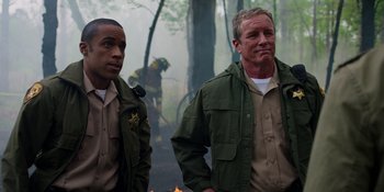 Movie still from “Teen Wolf: The Movie” (2023), directed by Russell Mulcahy – A couple of men standing next to each other near a fire; Medium shot, Over the shoulder angle