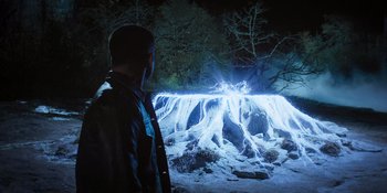 Movie still from “Teen Wolf: The Movie” (2023), directed by Russell Mulcahy – A man standing in front of a waterfall at night; Wide shot, High angle