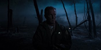 Movie still from “Teen Wolf: The Movie” (2023), directed by Russell Mulcahy – A man in a uniform holding a gun in the dark; Medium shot, Over the shoulder angle