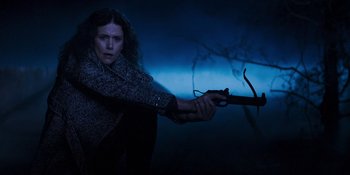 Movie still from “Teen Wolf: The Movie” (2023), directed by Russell Mulcahy – A woman is holding a gun in a dark room; Medium shot, Low angle