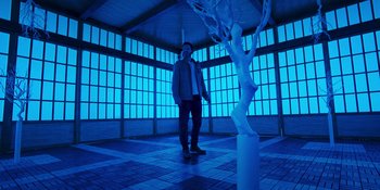 Movie still from “Teen Wolf: The Movie” (2023), directed by Russell Mulcahy – A man standing next to a white tree in a room; Wide shot, Low angle