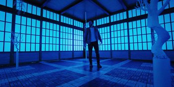 Movie still from “Teen Wolf: The Movie” (2023), directed by Russell Mulcahy – A man standing under an umbrella in a room; Wide shot, Low angle