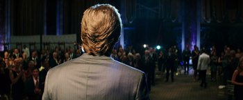 Movie still from “Teenage Mutant Ninja Turtles” (2014), directed by Jonathan Liebesman – A man in a gray suit is standing in front of a group of onlookers; Close Up shot, Over the shoulder angle