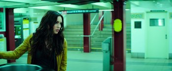Movie still from “Teenage Mutant Ninja Turtles” (2014), directed by Jonathan Liebesman – A woman in a yellow jacket standing in a train station; Medium shot, Over the shoulder angle
