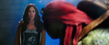 Movie still from “Teenage Mutant Ninja Turtles” (2014), directed by Jonathan Liebesman – A picture of a woman in front of a picture of a man in a red hat; Close Up shot, Over the shoulder angle