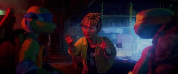 Movie still from “Teenage Mutant Ninja Turtles: Mutant Mayhem” (2023), directed by Jeff Rowe – A woman with a dreadlocks and a yellow jacket is standing in the dark; Medium shot, Over the shoulder angle