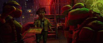 Movie still from “Teenage Mutant Ninja Turtles: Mutant Mayhem” (2023), directed by Jeff Rowe – A young boy holding a pizza box in front of a teenage mutant ninja turtle; Medium shot, High angle