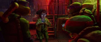 Movie still from “Teenage Mutant Ninja Turtles: Mutant Mayhem” (2023), directed by Jeff Rowe – A person in a green outfit holding a cell phone; Wide shot, Low angle
