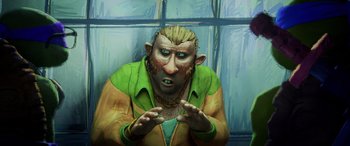 Movie still from “Teenage Mutant Ninja Turtles: Mutant Mayhem” (2023), directed by Jeff Rowe – A painting of a man wearing a green jacket and a gold chain necklace; Close Up shot, High angle