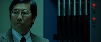 Movie still from “Terminator Salvation” (2009), directed by McG – A man in a suit and glasses is looking at the camera; Close Up shot, Over the shoulder angle