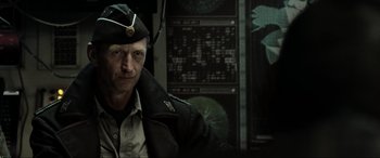 Movie still from “Terminator Salvation” (2009), directed by McG – A man in a military uniform is standing in front of a wall; Close Up shot, Over the shoulder angle