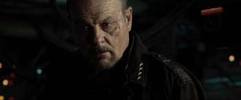 Movie still from “Terminator Salvation” (2009), directed by McG – An older man wearing a black shirt and looking at the camera; Close Up shot, Low angle