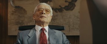 Movie still from “Tetris” (2023), directed by Jon S. Baird – An older man in a suit and tie sitting in an office chair; Close Up shot, Low angle