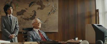 Movie still from “Tetris” (2023), directed by Jon S. Baird – An older man sitting at a desk in front of a painting; Medium shot, Low angle