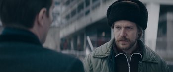 Movie still from “Tetris” (2023), directed by Jon S. Baird – A man wearing a hat and a jacket talking to another man; Close Up shot, Over the shoulder angle