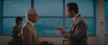 Movie still from “Tetris” (2023), directed by Jon S. Baird – Two men in suits are holding guns in front of a window; Medium shot, Over the shoulder angle