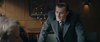 Movie still from “Tetris” (2023), directed by Jon S. Baird – A man sitting in a chair wearing a suit and tie; Medium shot, Low angle