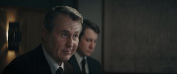 Movie still from “Tetris” (2023), directed by Jon S. Baird – A man in a suit and tie next to another man in a suit and tie; Close Up shot, Over the shoulder angle