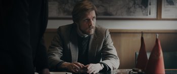 Movie still from “Tetris” (2023), directed by Jon S. Baird – A man sitting at a table in front of a map; Medium shot, Over the shoulder angle