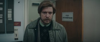 Movie still from “Tetris” (2023), directed by Jon S. Baird – A man in a green jacket standing next to a door; Medium shot, Low angle