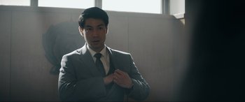 Movie still from “Tetris” (2023), directed by Jon S. Baird – A man in a gray suit and a white shirt is fixing his tie; Medium shot, Over the shoulder angle