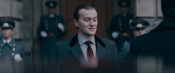 Movie still from “Tetris” (2023), directed by Jon S. Baird – A man wearing a suit and tie standing in front of a building; Close Up shot, Over the shoulder angle