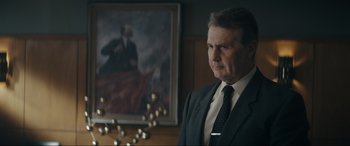 Movie still from “Tetris” (2023), directed by Jon S. Baird – A man wearing a suit and tie in front of a painting; Medium shot, Low angle