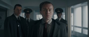 Movie still from “Tetris” (2023), directed by Jon S. Baird – A man in a suit and tie standing in front of two other men; Close Up shot, Low angle