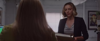 Movie still from “That's Amor” (2022), directed by Shaun Paul Piccinino – A woman sitting in front of a mirror looking at a book; Medium shot, Over the shoulder angle