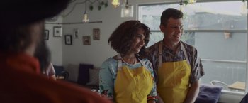 Movie still from “That's Amor” (2022), directed by Shaun Paul Piccinino – A man and a woman wearing aprons standing next to each other; Medium shot, Over the shoulder angle