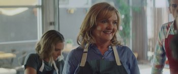 Movie still from “That's Amor” (2022), directed by Shaun Paul Piccinino – A woman wearing an apron smiles at the camera; Close Up shot, Over the shoulder angle