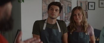 Movie still from “That's Amor” (2022), directed by Shaun Paul Piccinino – A man wearing an apron standing next to a woman wearing an apron; Close Up shot, Over the shoulder angle