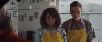 Movie still from “That's Amor” (2022), directed by Shaun Paul Piccinino – A woman wearing an apron standing next to a man wearing an apron; Medium shot, Low angle