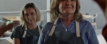 Movie still from “That's Amor” (2022), directed by Shaun Paul Piccinino – Two women wearing aprons are standing next to each other; Close Up shot, Over the shoulder angle
