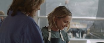 Movie still from “That's Amor” (2022), directed by Shaun Paul Piccinino – A woman in an apron smiles at another woman; Close Up shot, Over the shoulder angle