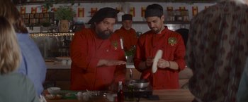 Movie still from “That's Amor” (2022), directed by Shaun Paul Piccinino – A group of men standing in a kitchen preparing food; Medium shot, Over the shoulder angle