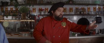 Movie still from “That's Amor” (2022), directed by Shaun Paul Piccinino – A man wearing a red jacket and a black hat; Medium shot, Low angle