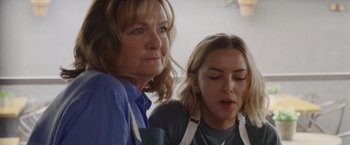 Movie still from “That's Amor” (2022), directed by Shaun Paul Piccinino – A woman and a woman wearing white aprons look at each other; Close Up shot, Over the shoulder angle